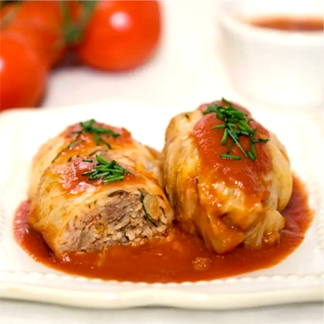 Two holubki under tomato sauce, one cut open to show the filling