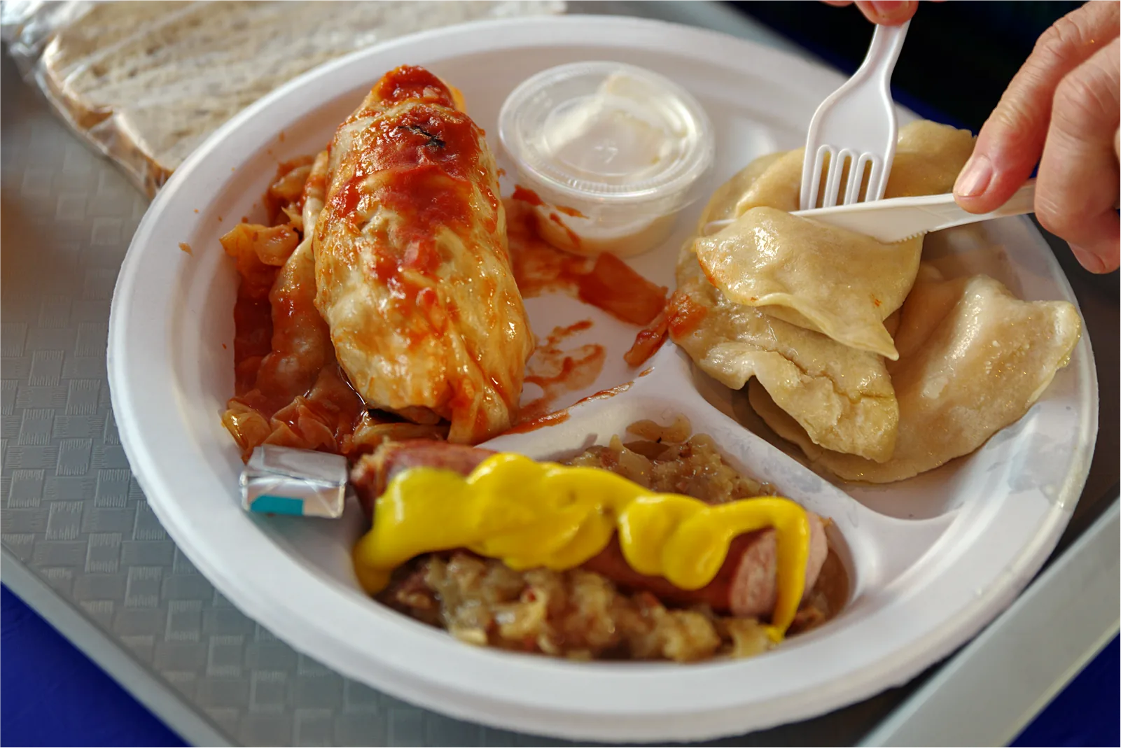 An ethnic platter on a tray at the tent: a sauced holubki, two perohi, a kielbasa with sauerkraut and mustard, sour cream, and rye bread